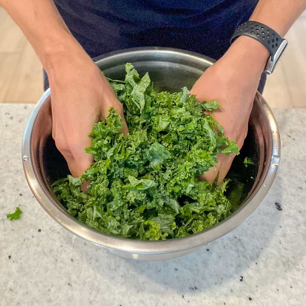 A woman's hands massaging kale in a mixing bowl.