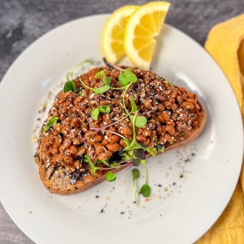 Natto avocado toast on a plate with fresh sliced lemon on the side.