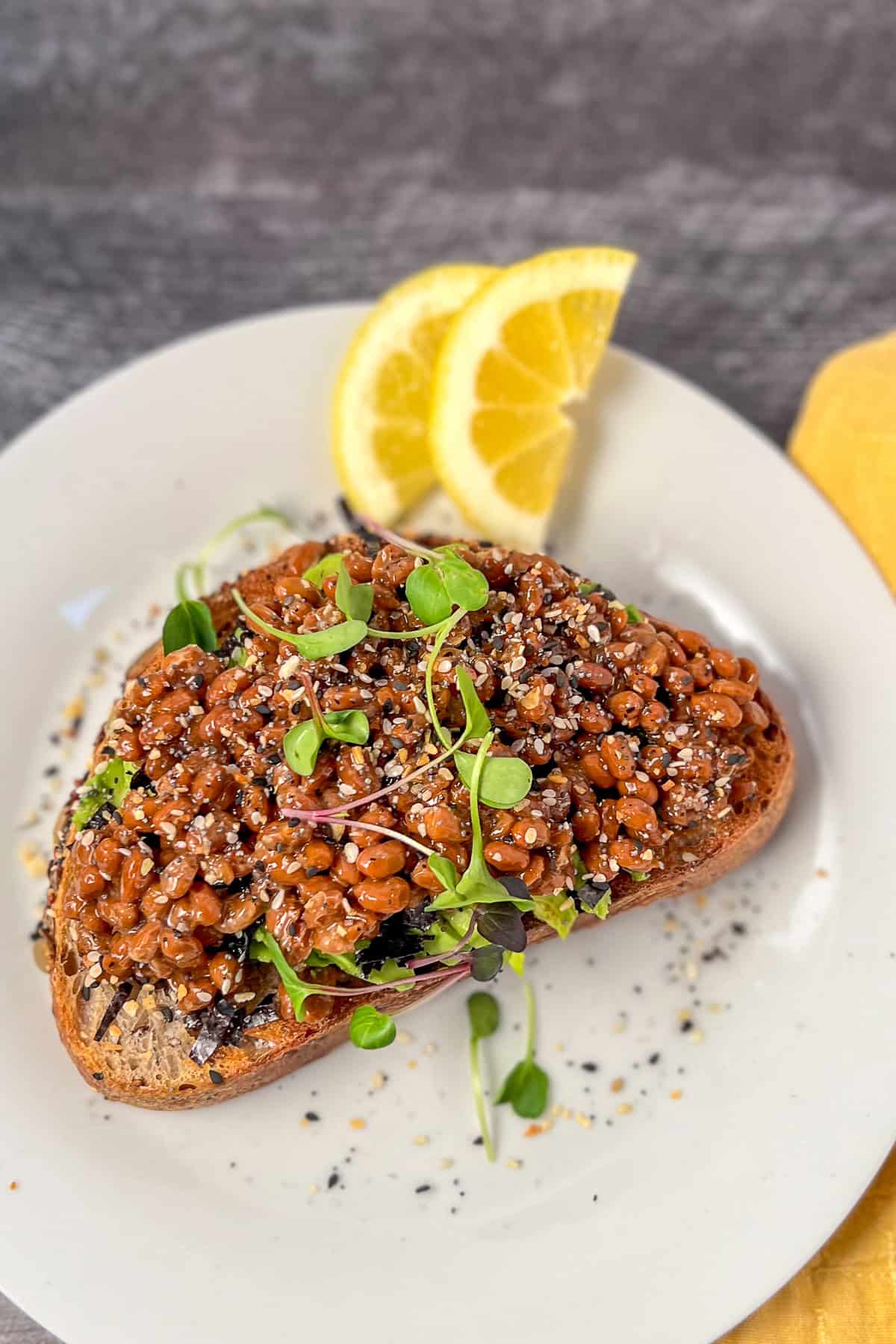 Natto avocado toast with microgreens and fresh lemon slices on a plate.