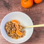 Orange walnut granola in a bowl with almond milk and topped with orange segments.