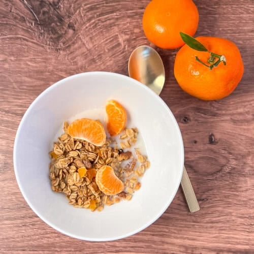 Orange walnut granola in a bowl with almond milk and mandarin orange segments on top.
