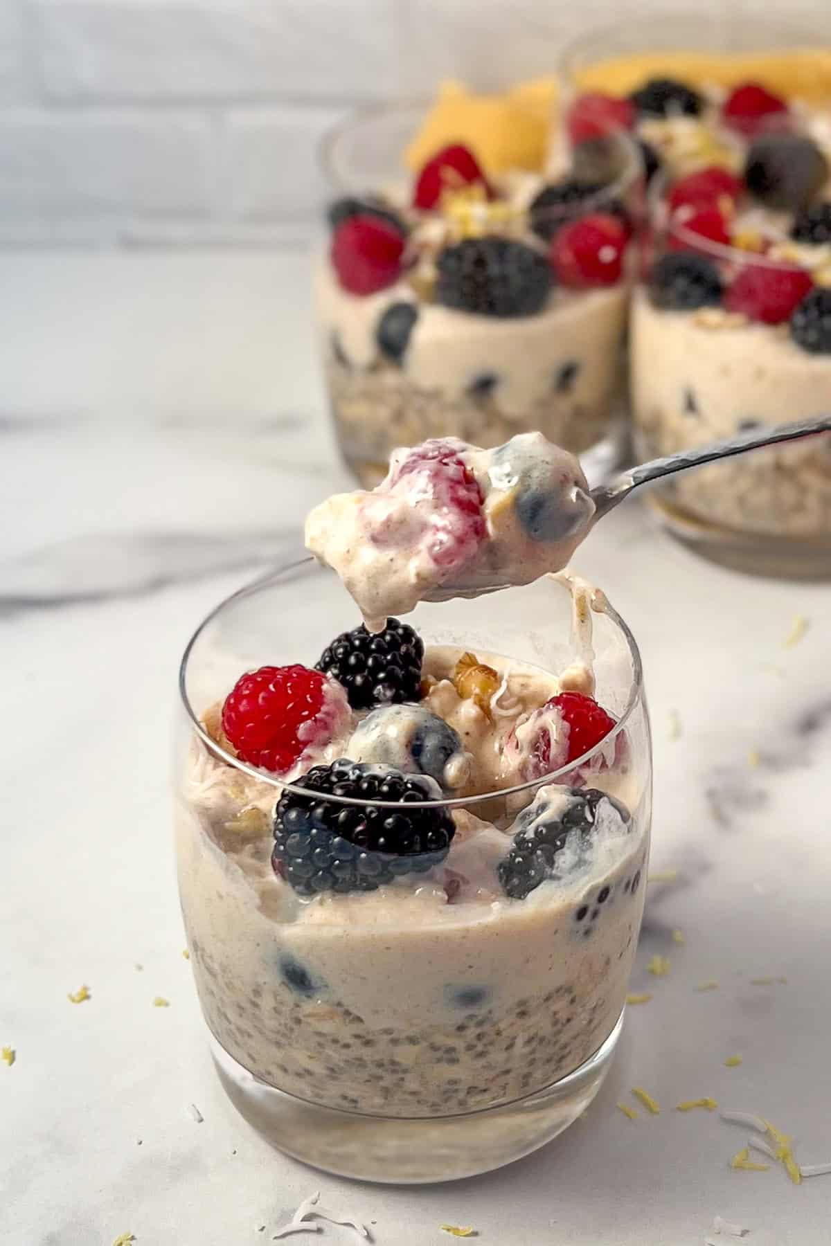 Overnight oats parfait with mixed berries in a glass with a spoon lifting out a bite.