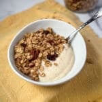 Pumpkin spice granola in a bowl with spoon and soy yogurt.