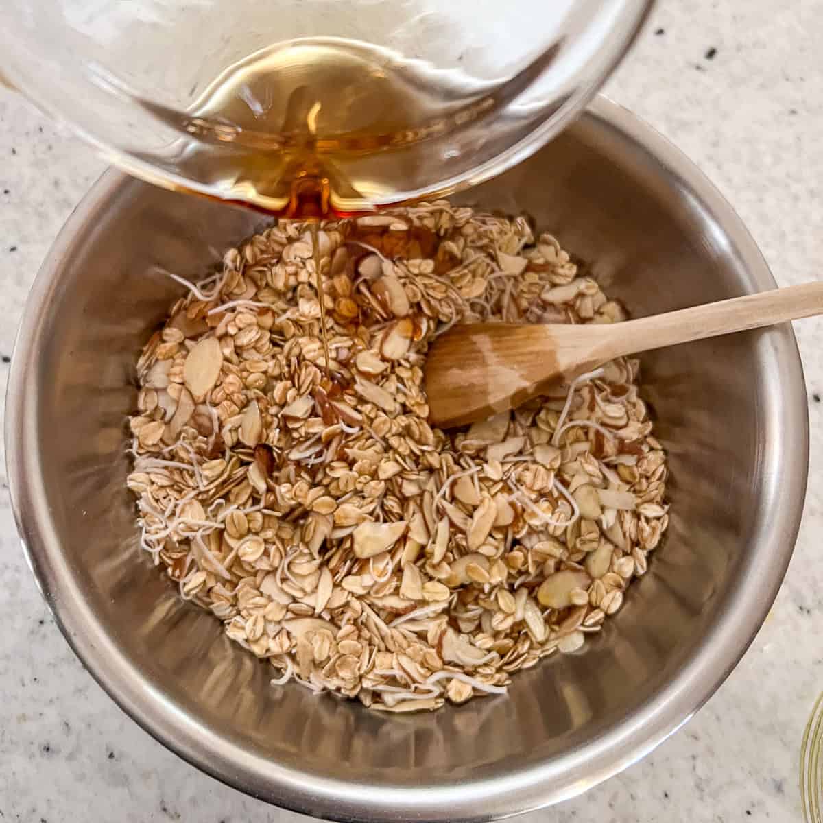 Maple syrup being added to the mixing bowl for vanilla almond granola.