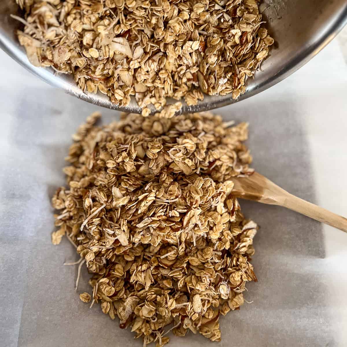 Granola mixture being added to the parchment-lined baking sheet.