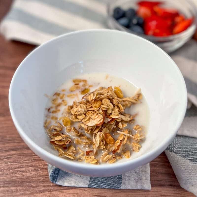 A bowl of vanilla almond granola with fresh berries blurred in the background.