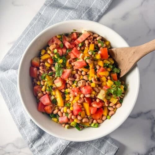 Black eyed peas corn salad in a large bowl with a wooden serving spoon.