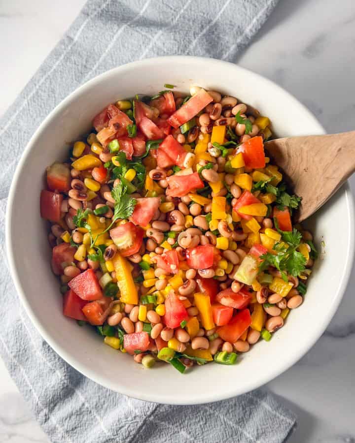Black eyed peas corn salad in a large bowl with a wooden serving spoon.