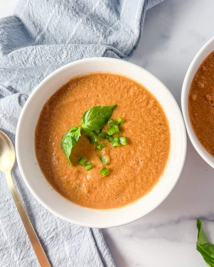Italian gazpacho in a bowl topped with fresh basil and a spoon on the side.
