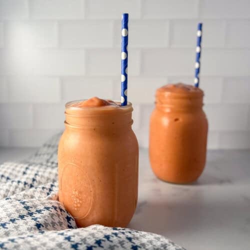Two sunrise sunset smoothies in mason jars with straws.