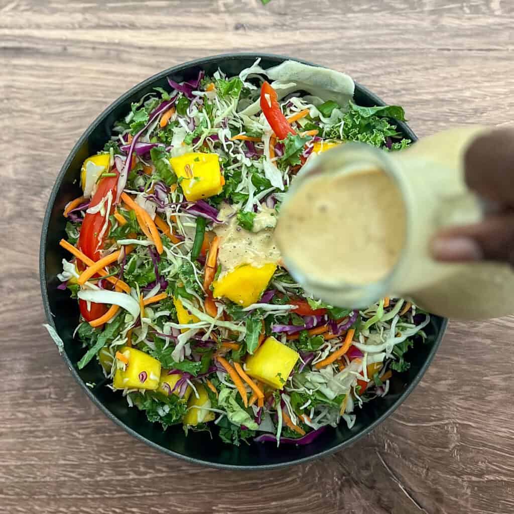 A bowl of mixed raw vegetables and mango with a cashew sauce being pour over it.