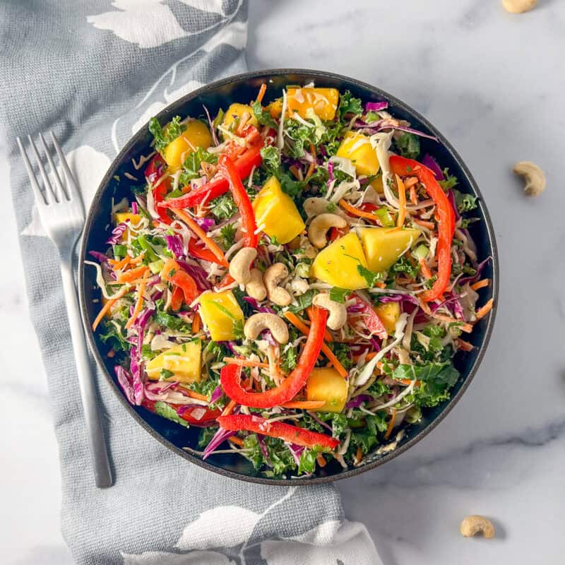 A mango coleslaw salad in a bowl with a variety of vegetables and creamy cashew sauce.