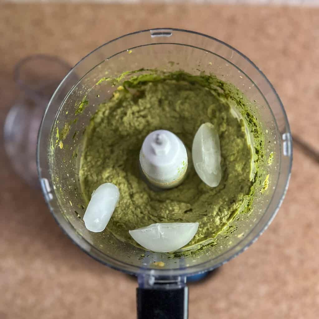 Matcha hummus in a food processor with three ice cubes.
