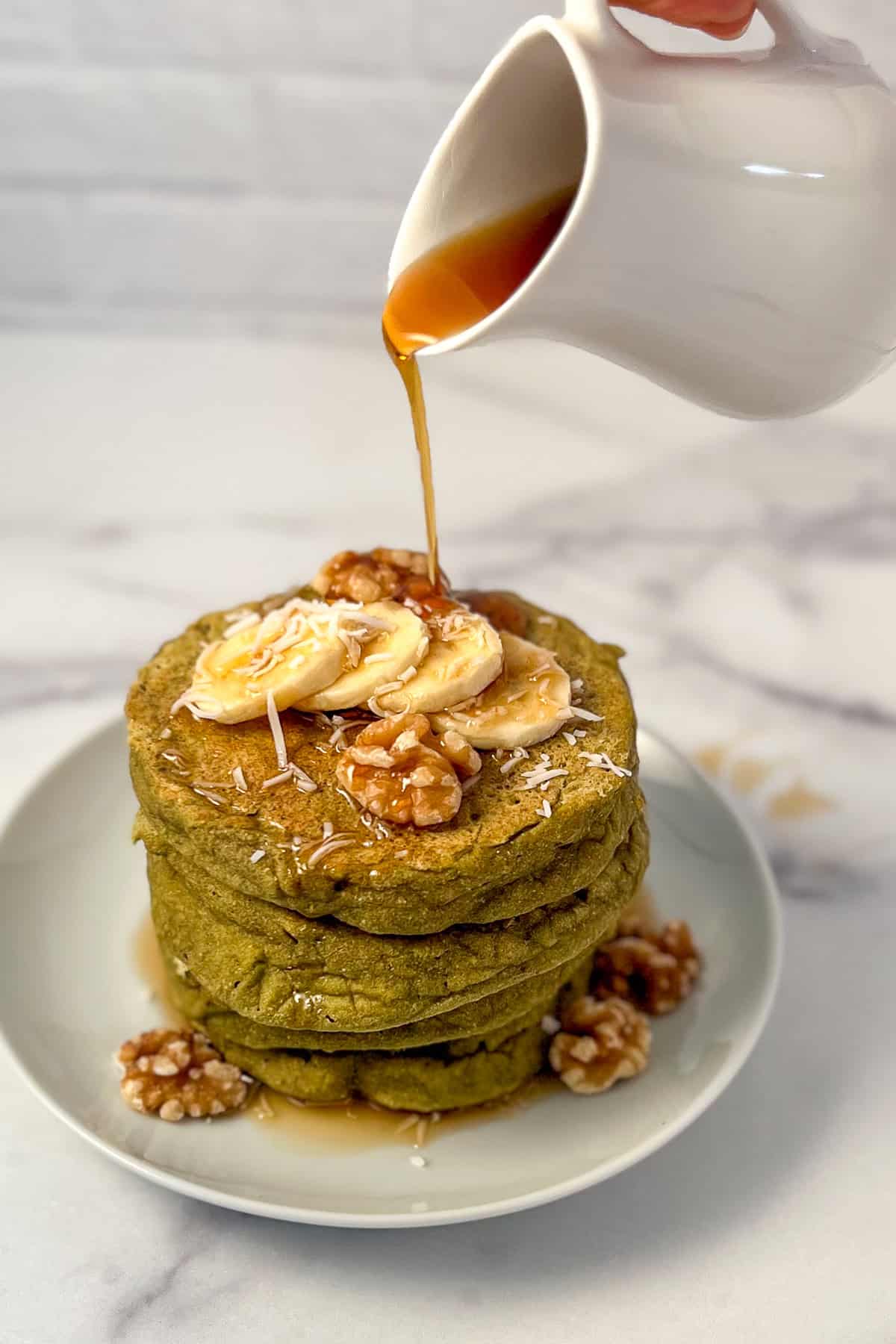A stack of matcha pancakes with maple syrup being poured on top.