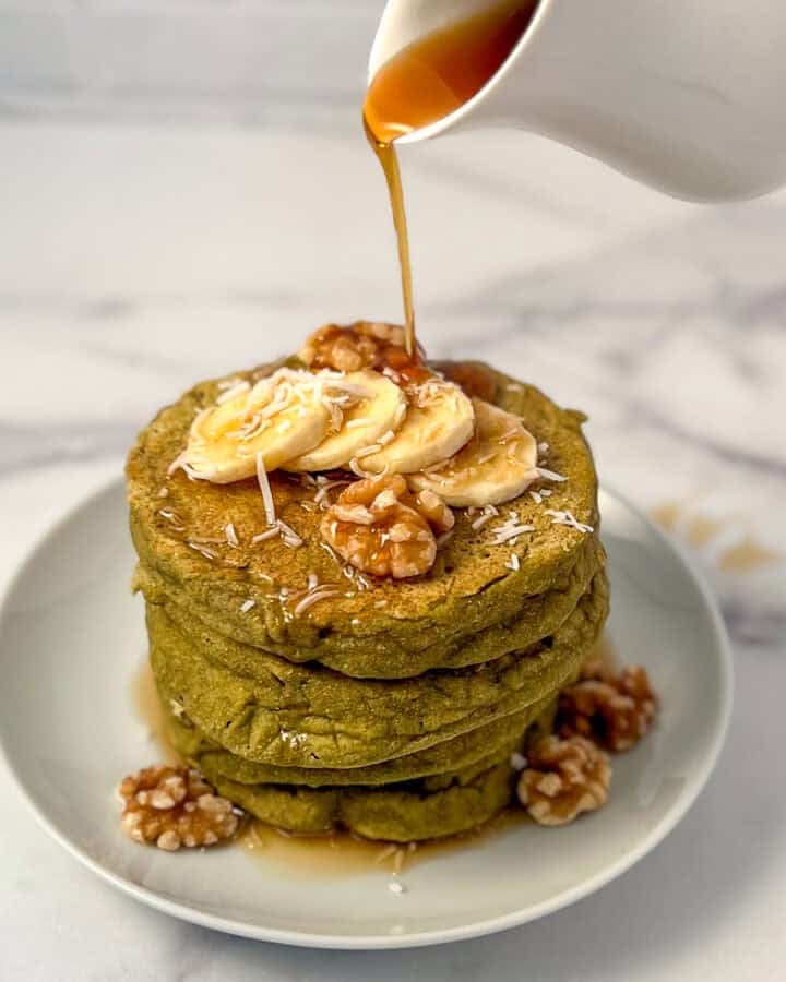A stack of matcha pancakes with syrup being poured on top.