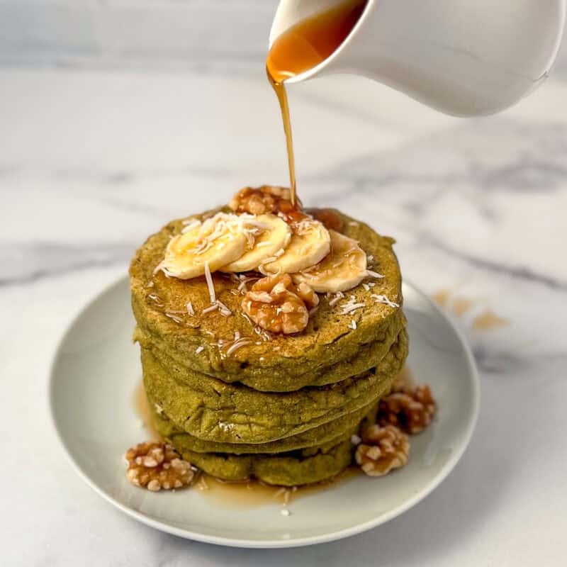 A stack of matcha pancakes with syrup being poured on top.