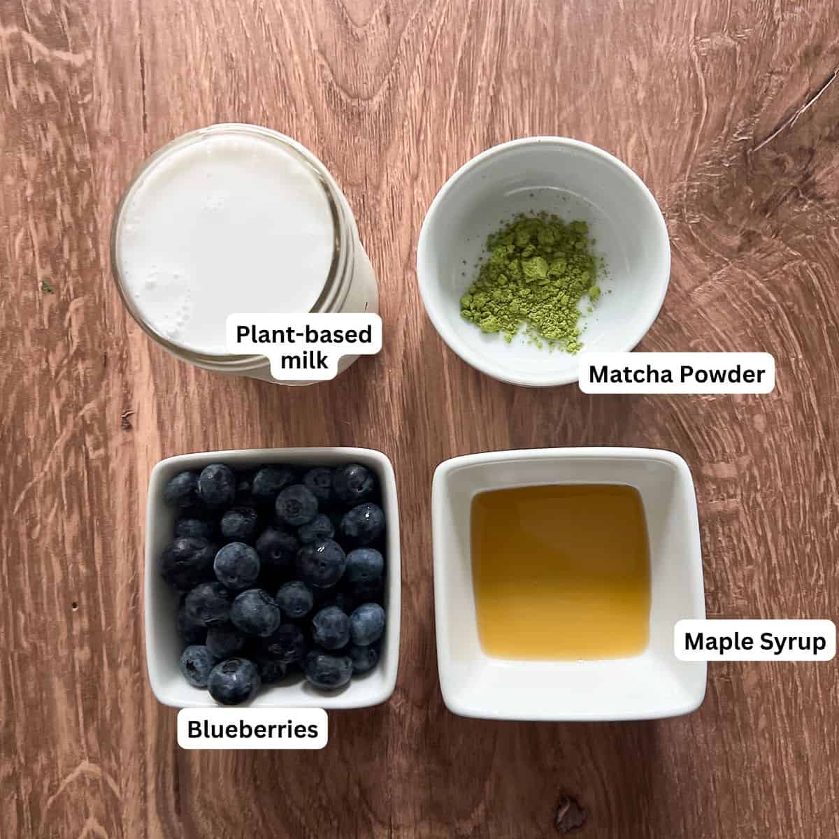A bowl of blueberries, cup of plant based milk, a bowl of matcha powder and a bowl of maple syrup. 
