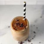 A mason jar filled with a banana smoothie with coffee with a straw.