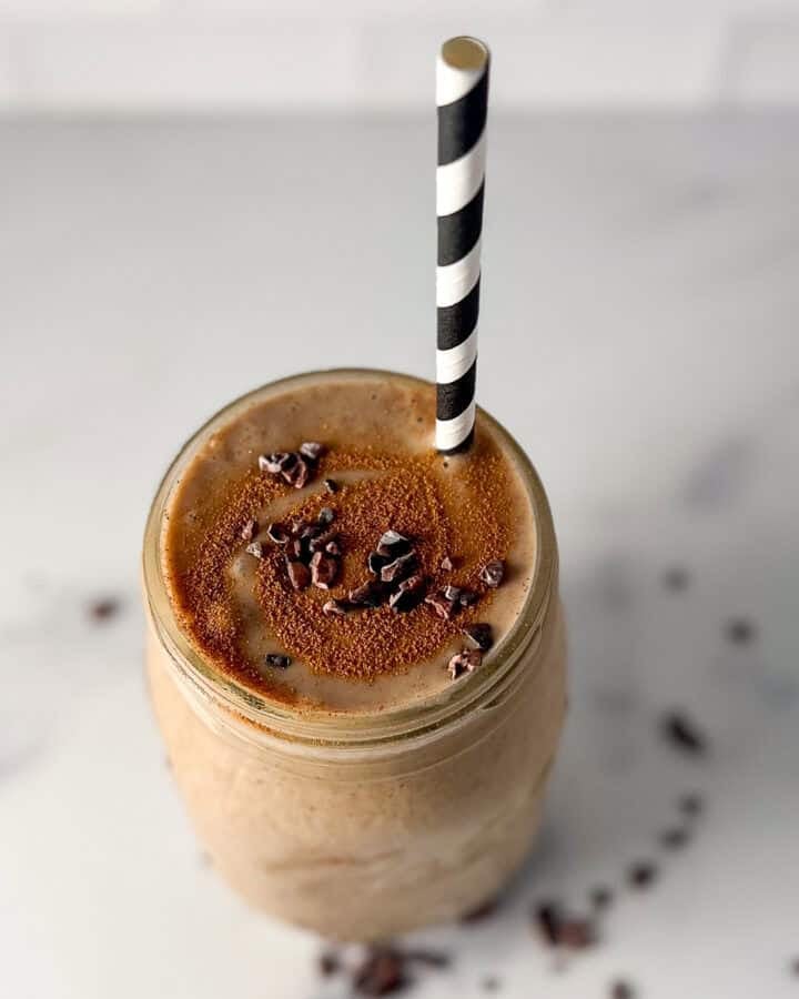 A mason jar filled with a banana smoothie with coffee with a straw.