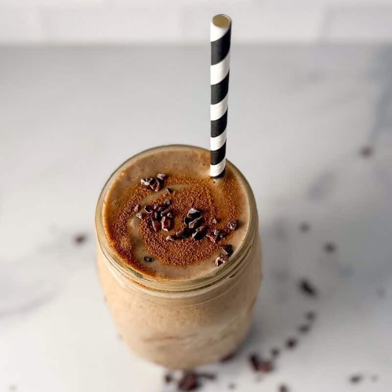 A mason jar filled with a banana smoothie with coffee with a straw.