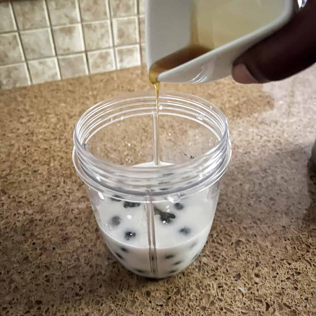A cup of blueberries in plant based milk with a pouring of maple syrup into the cup.