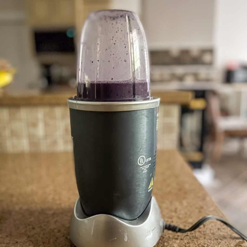 A bullet blender with blended blueberries, planted based milk and maple syrup.