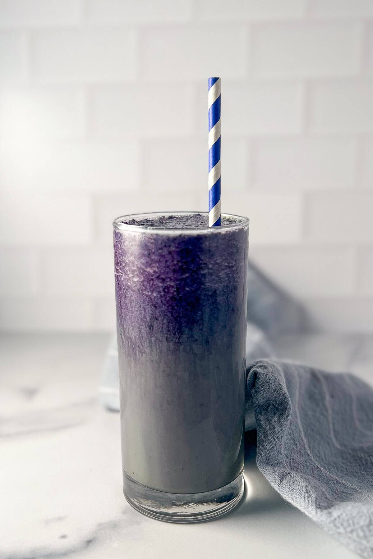 Tall glass of blueberry matcha latte with a straw.