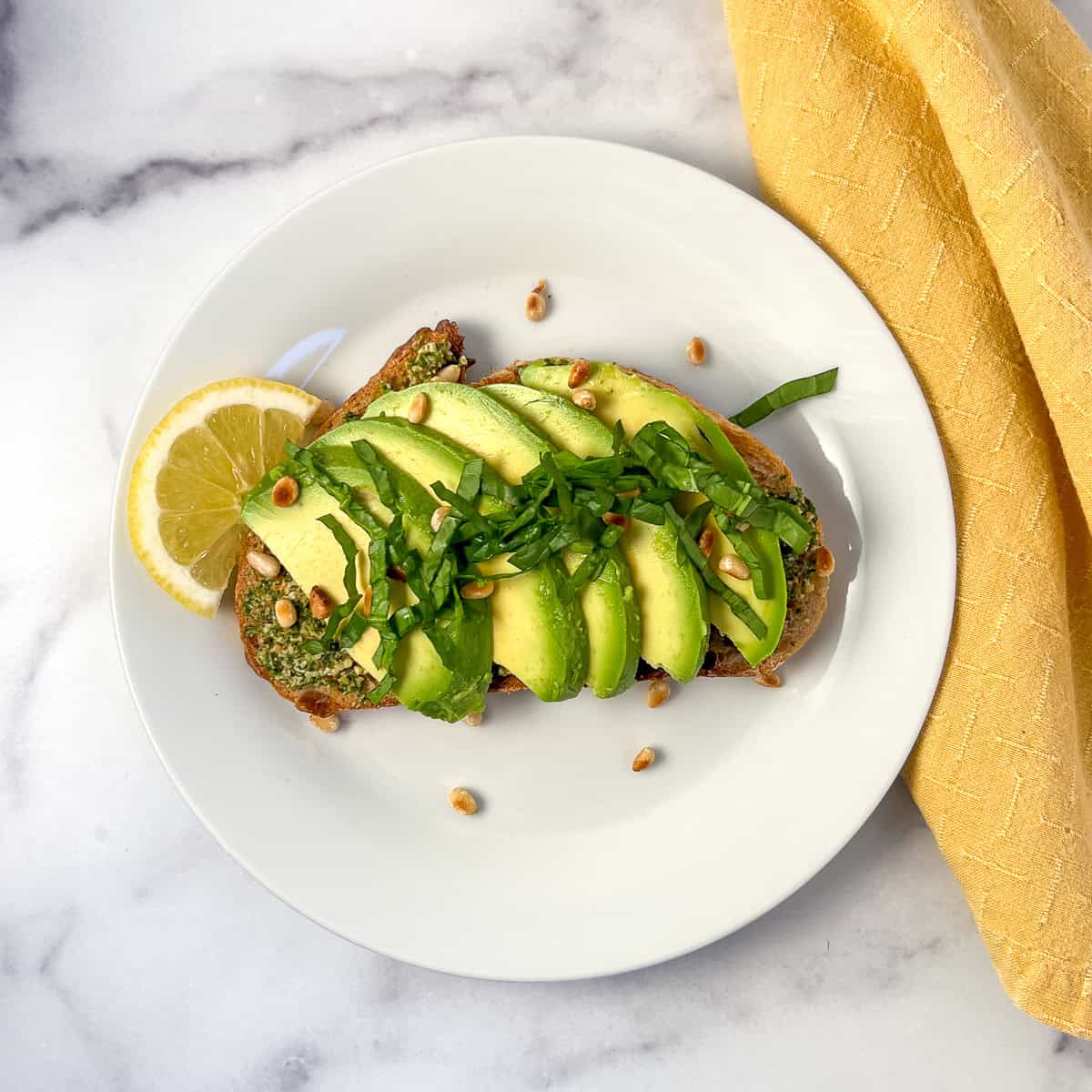 One piece of pesto avocado toast on a plate topped with chopped spinach and toasted pine nuts.