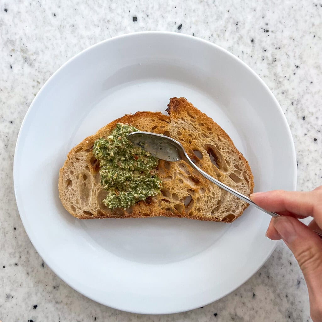Spreading  arugula basil pesto onto toasted bread.