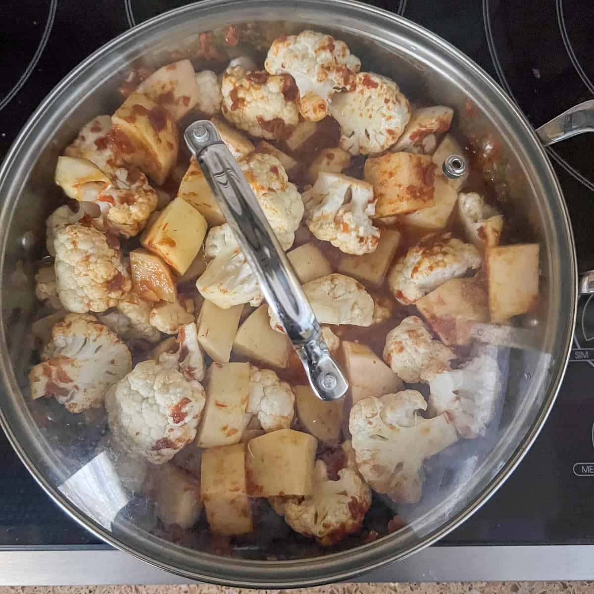 A pan with cauliflower, potatoes, crushed tomatoes and various indain inspired spices.