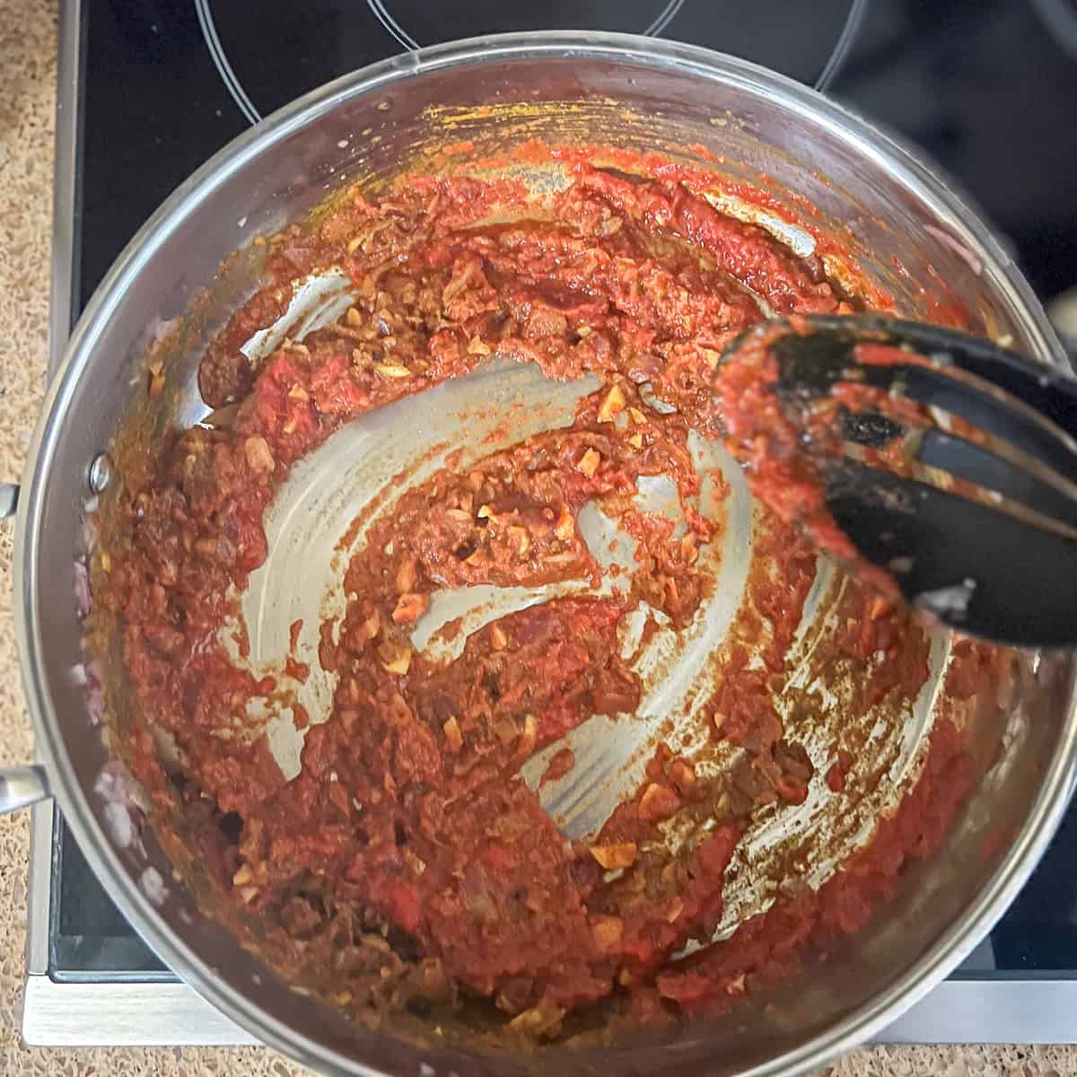 A variety of seasonings in a pan with onions and garlic and crushed canned tomatoes.