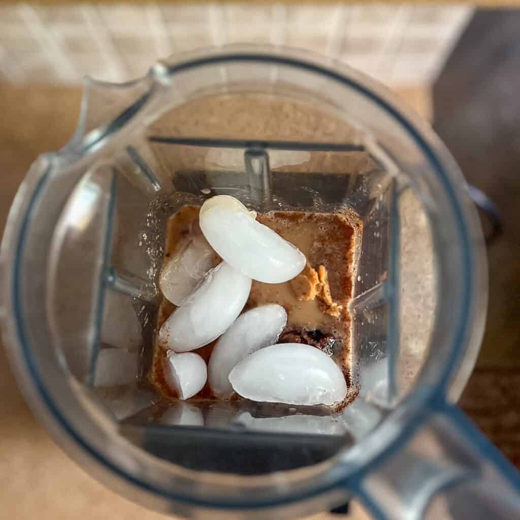 A blender filled with banana, flaxseed, dates, vanilla bean powder, cinnamon, soy milk, brewed coffee and soy milk.