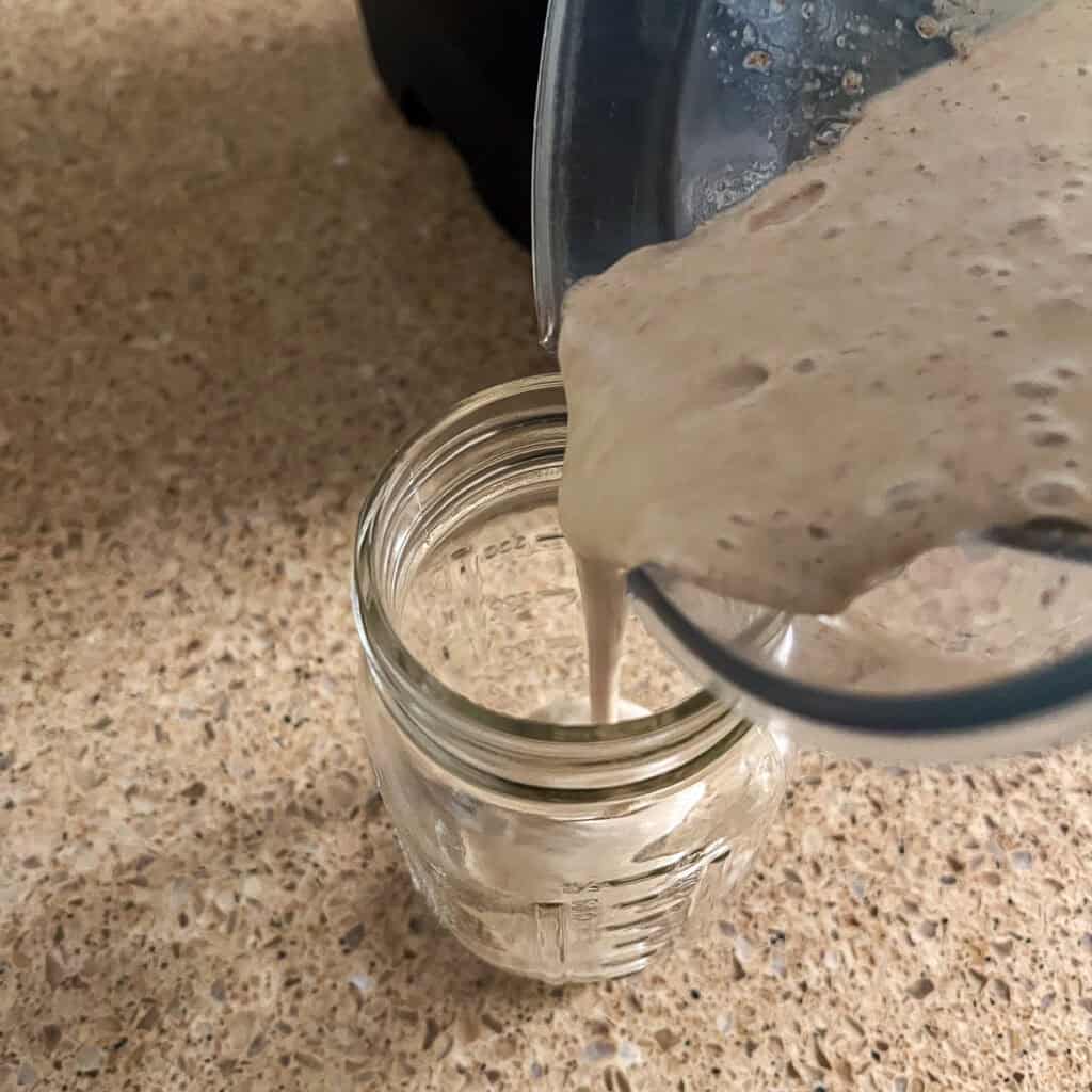 A banana smoothie with coffee blended and being poured into a glass.