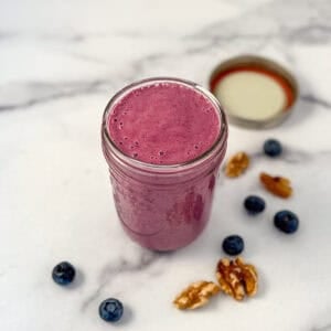 Blueberry vinaigrette dressing in a mason jar with loose blueberries and walnuts scattered on the side.