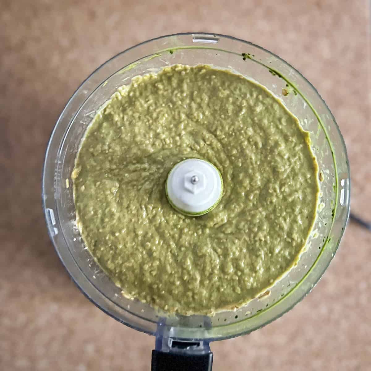 A food processor blended with ingredients to include chickpeas, dates raisins, coconut milk, cashew butter, matcha powder, vanilla extract, baking powder and soda and salt.