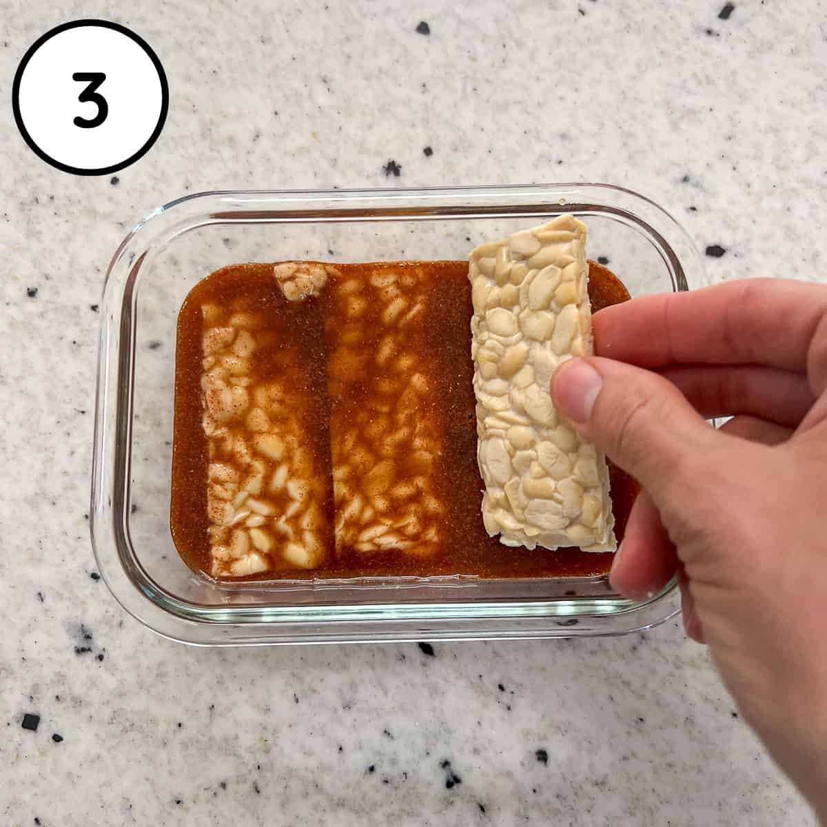 Tempeh slabs being added to the dish with marinade.