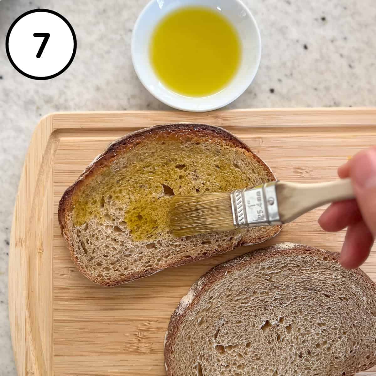 Olive oil being brushed on one side of a slice of rye bread.