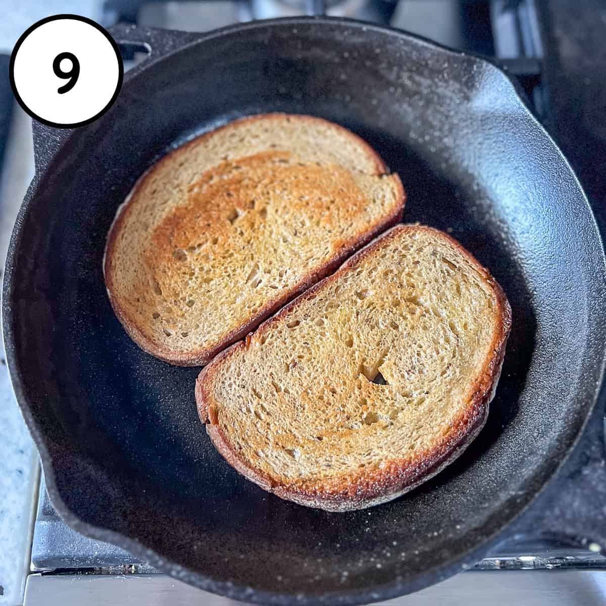 Two slices of rye bread toasting in a cast iron skillet.