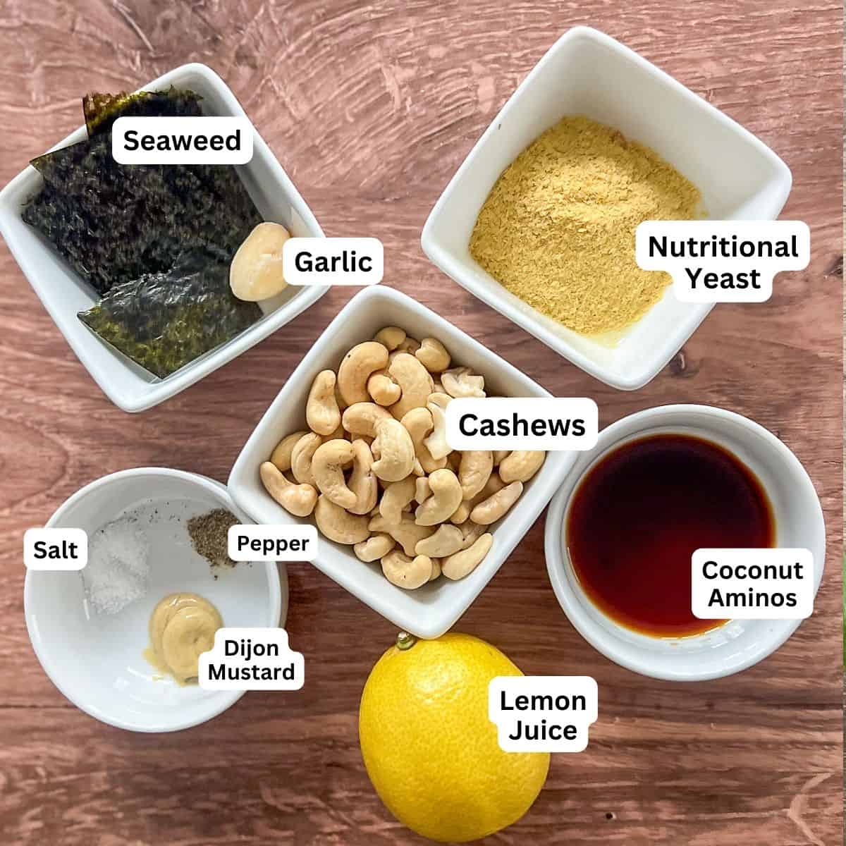 Small bowls of pepper, salt, Dijon mustard, coconut aminos, nutritional yeast, cashews, seaweed, lemon and garlic.