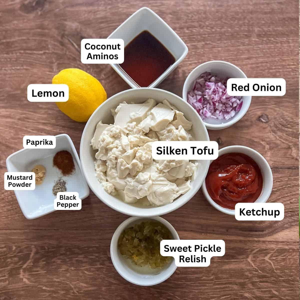 Small bowl of ketchup, silken tofu, chopped onions, sweet pickle relish, a lemon a bowl with paprika, pepper and mustard powder and coconut amions.