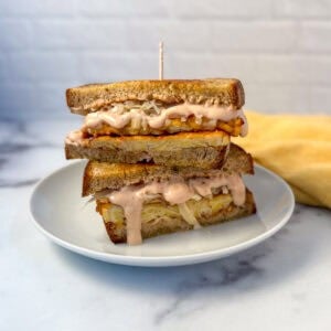 Tempeh Reuben Sandwich sliced in half on a plate with sauce dripping down.