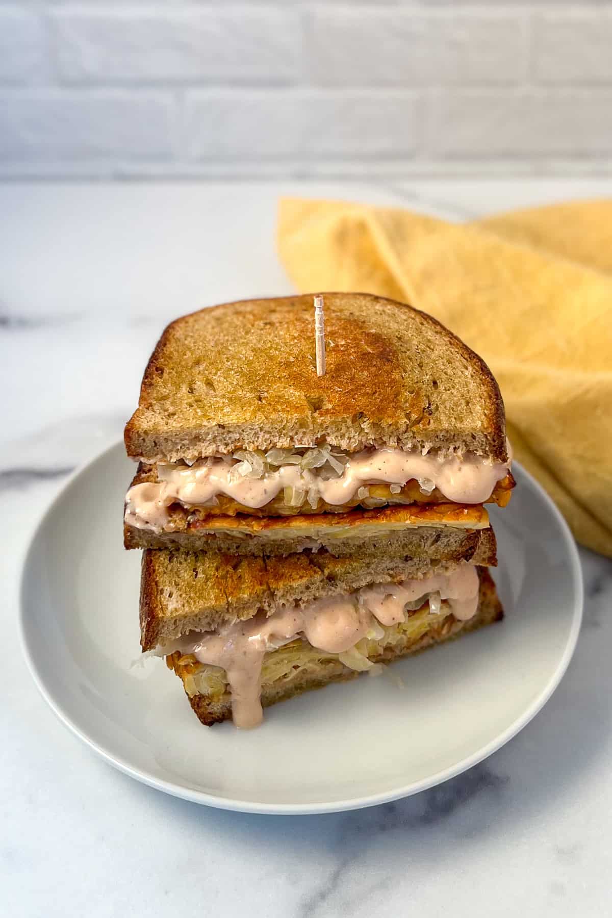Tempeh reuben sandwich stacked on a plate with a toothpick, napkin on the side.