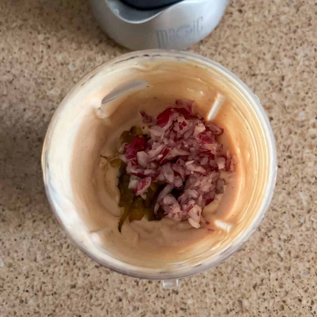 A blender with vegan thousand island dressing with minced red onion and relish.
