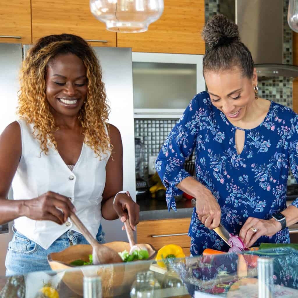 Two women cooking in the kitchen, smiling.