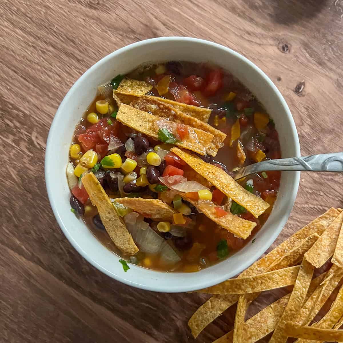 Black bean tortilla soup in a bowl with a spoon; tortilla strips on top and on the side.