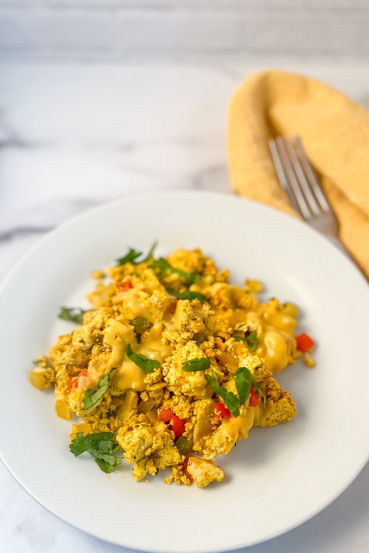 Cheesy tofu scramble topped with fresh herbs on a plate.