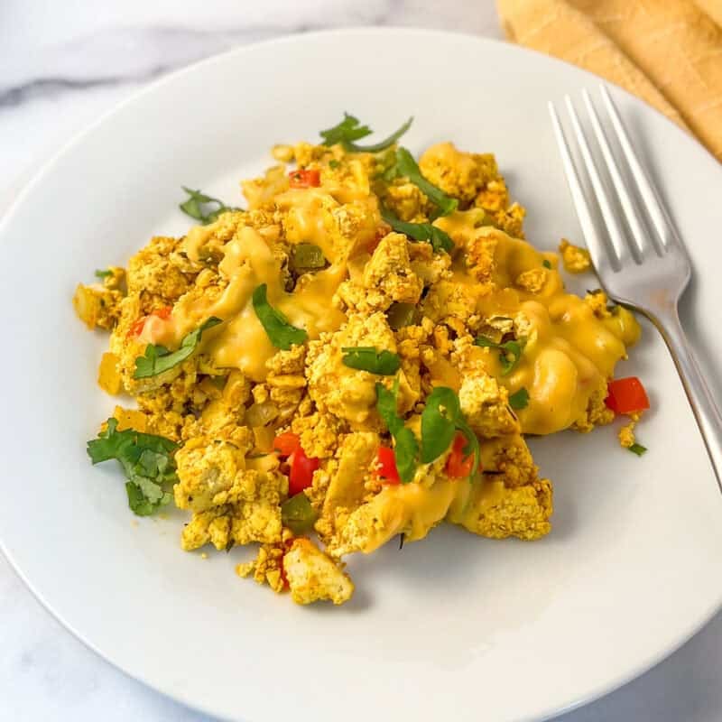 Cheesy tofu scramble on a plate with a fork on the side.