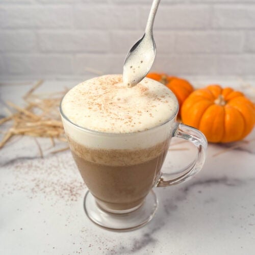Pumpkin spice latte in a glass mug with spoon coming out.
