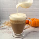 Pumpkin spice latte in a glass mug with foamy soy milk being poured on top.