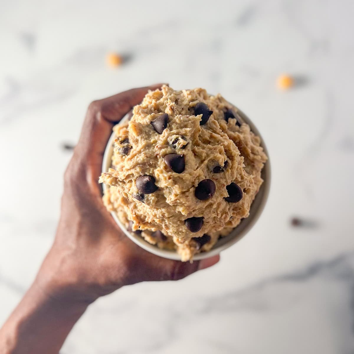 A woman's hand holding a bowl of vegan chocolate chip cookie dough.
